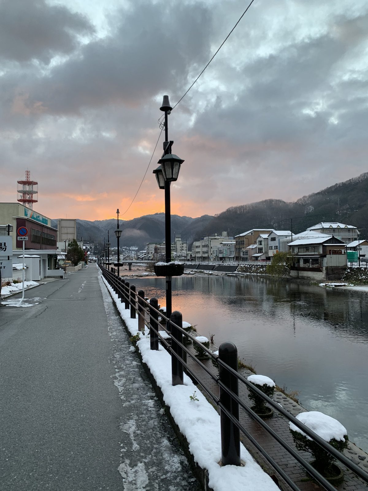 A riverside path and street lamps under a light covering of snow at dawn in a mountain town